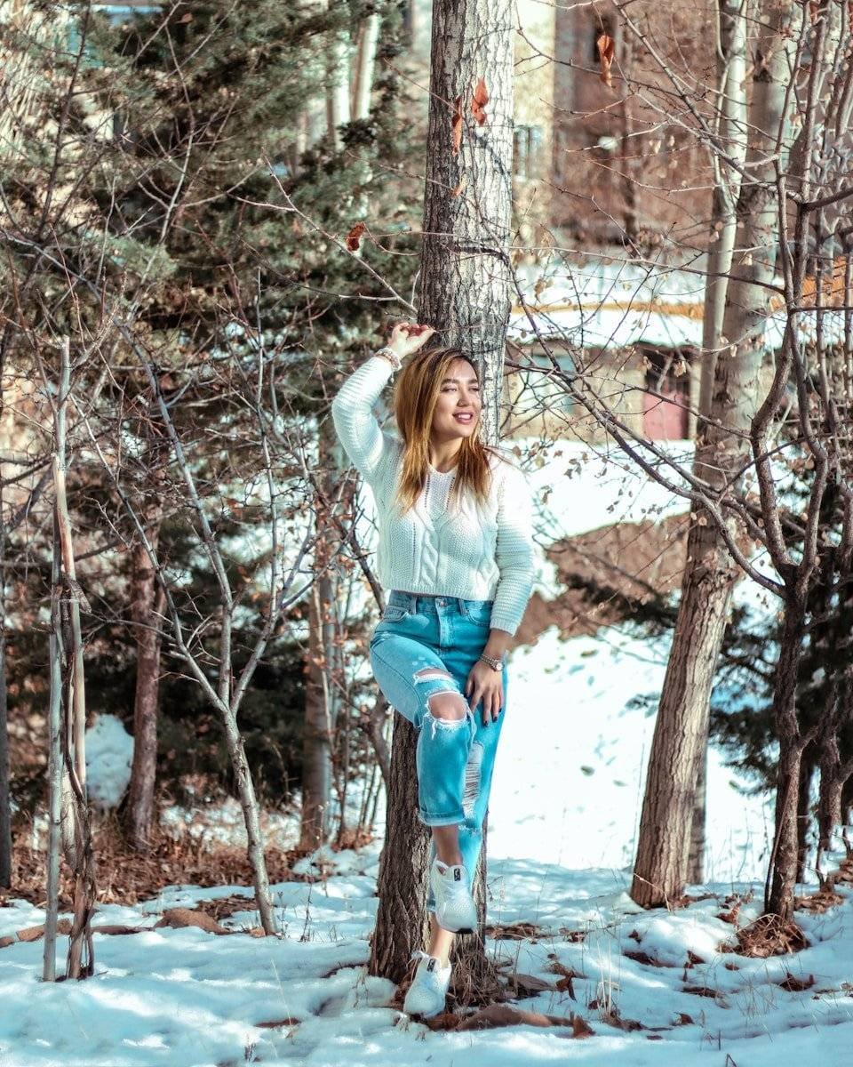 woman in white sweater leaning on tree